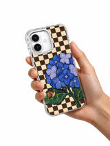 Hand holding the blue hydrangea, snail and checkerboard iPhone 17 case.