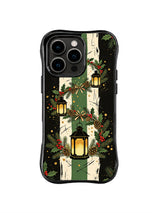 Birchlight Lantern Trail pattern on a black iPhone 14 Pro case with ivory birch trunks, hanging gold lanterns, holly leaves, red berries and deep green brushwork