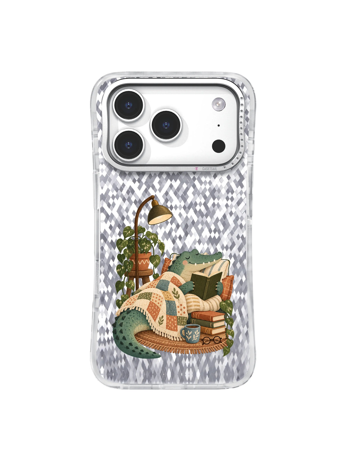 Muted teal crocodile reading under a patchwork blanket on an iPhone 17 Pro case illustration.