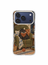 Charcoal cat reading a terracotta book in an olive armchair on an iPhone 17 Pro case