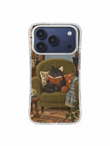 Charcoal cat reading among cushions with a yarn ball trailing from an olive chair on an iPhone 17 Pro case