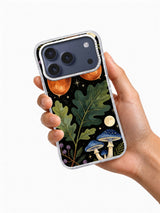 Hand holding a phone case printed with copper acorns, green oak leaves, blue mushrooms, and ivory moon details