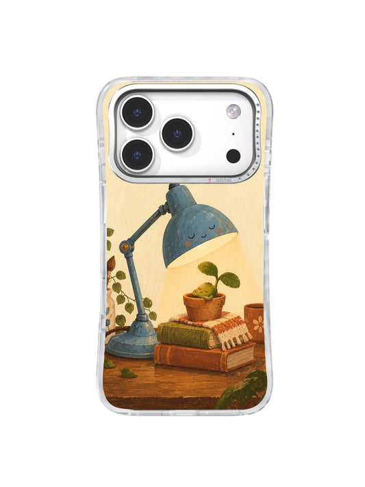 Blue table lamp sheltering a small green seedling on old books, illustrated on an iPhone 17 Pro case