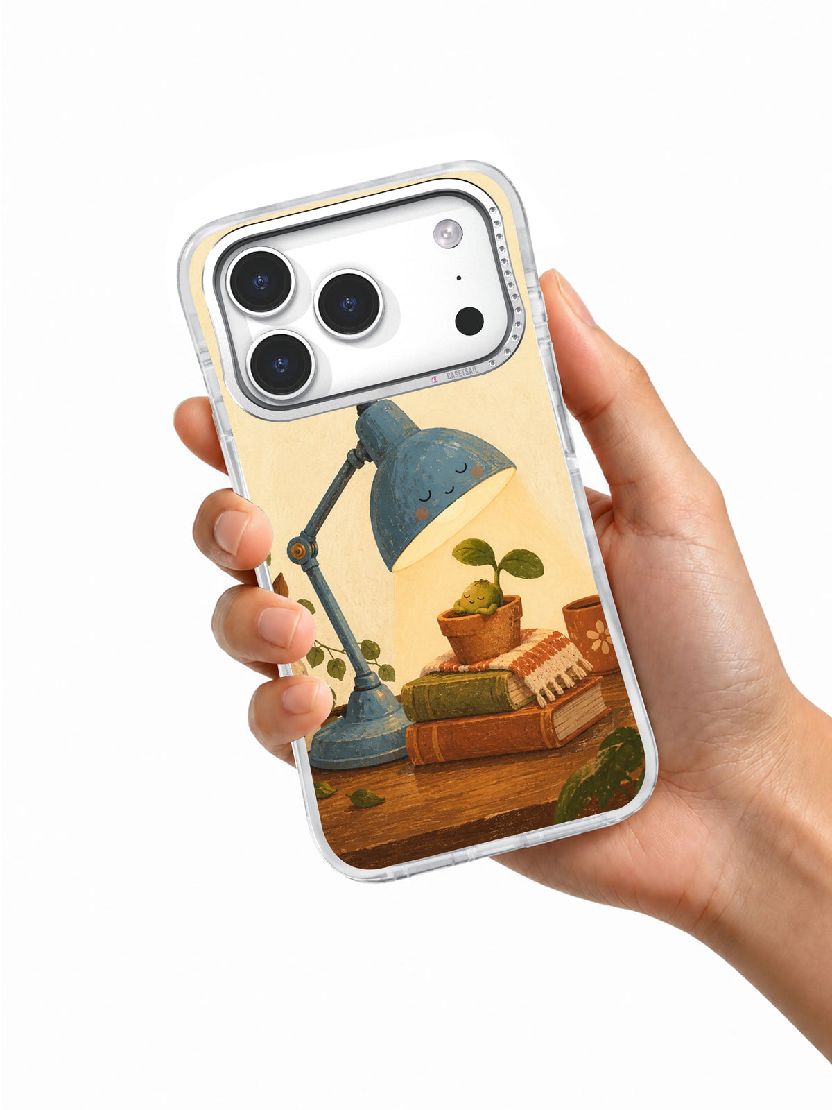 Hand holding a clear iPhone 17 Pro case decorated with a blue lamp sheltering a seedling