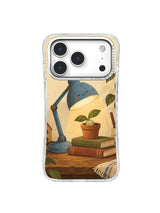 Blue lamp bending toward green leaves above terracotta and olive books on an iPhone 17 Pro case