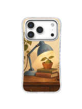 Small potted seedling guarded by a blue lamp over stacked books on an iPhone 17 Pro case