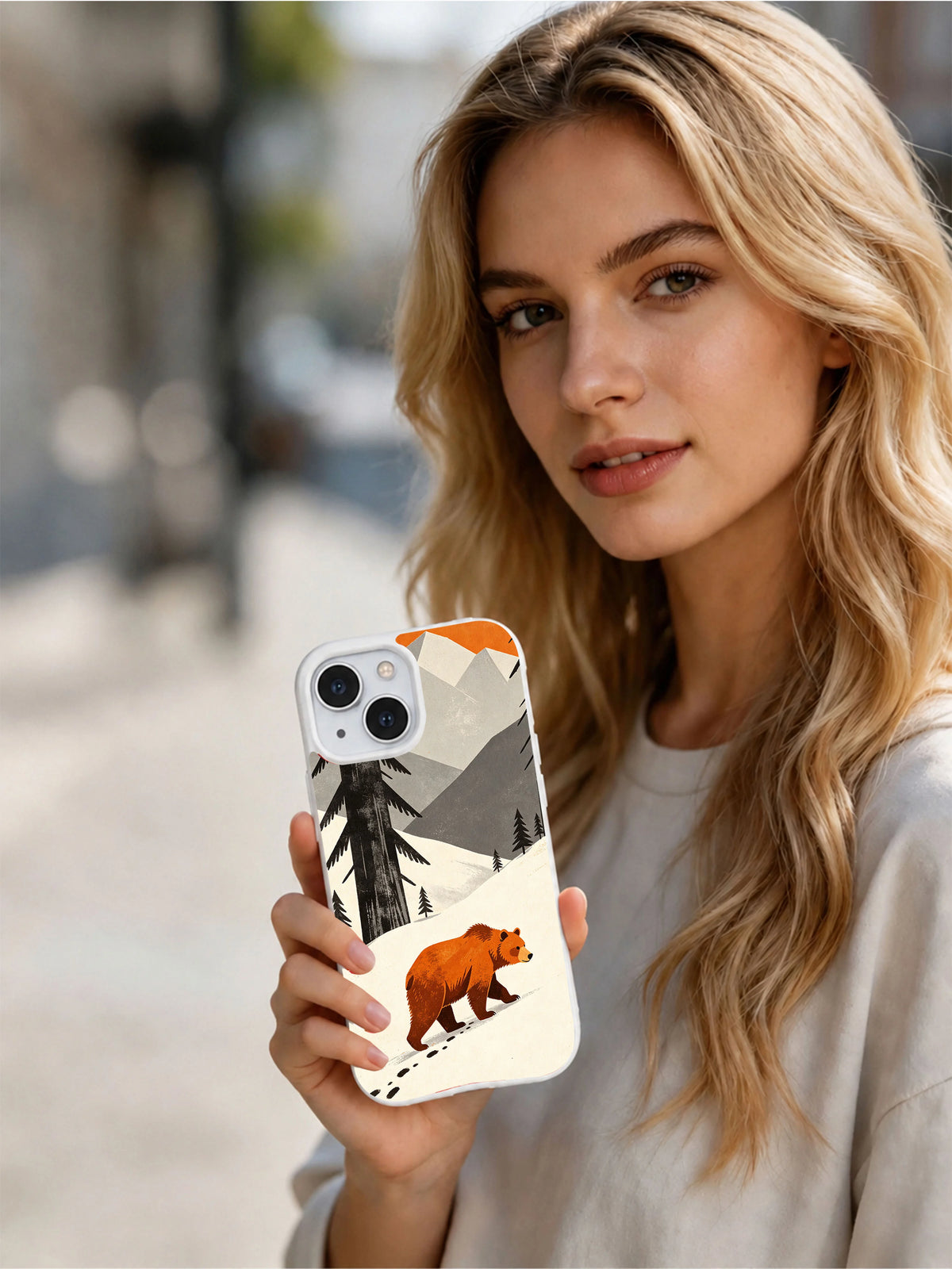 Woman holding an iPhone 13 case featuring the Orange Bear Valley artwork