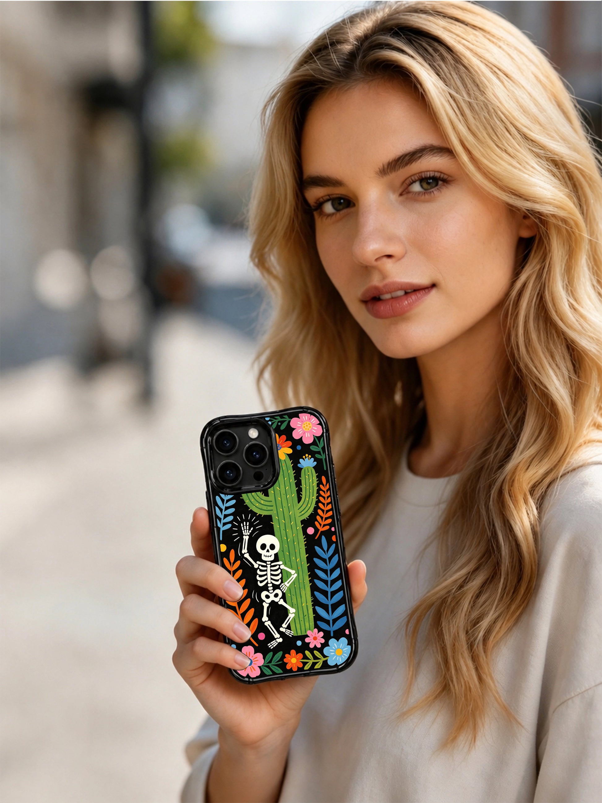 PhoneCasing iPhone 16 pro max Case with a playful skeleton peeking from behind a large blooming cactus, surrounded by bright flowers and green foliage, whimsical folk art on black iPhone 16 pro max casing.
