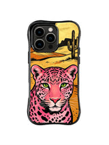 Close-up pink leopard face with green eyes below a golden desert and black cactus silhouettes on iPhone 13 Pro Max case