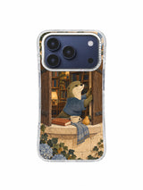 Otter in a dusty blue wrap closing cocoa shutters beside books and a pear on an iPhone 17 Pro case