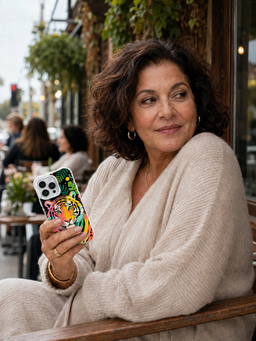 Adult woman at a café holding the Rainbow Jungle Tiger iPhone 13 Pro Max case with Leaf and Sunspot Tiger artwork