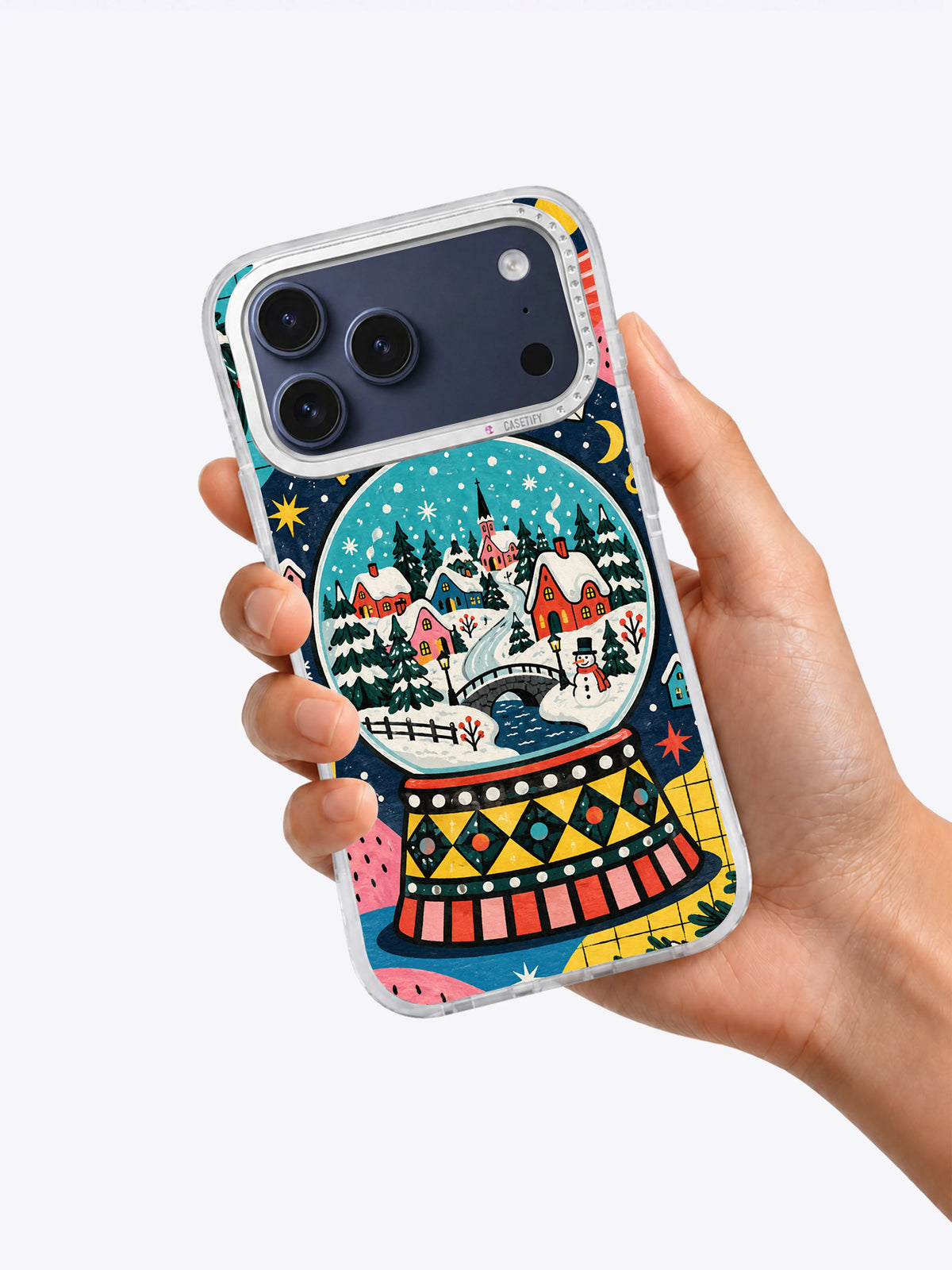 Snow Globe Town iPhone 17 Pro Max case held in one hand showing the colorful winter village artwork