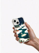 Hand holding the clear-edge Swan's Christmas Lake iPhone 14 case
