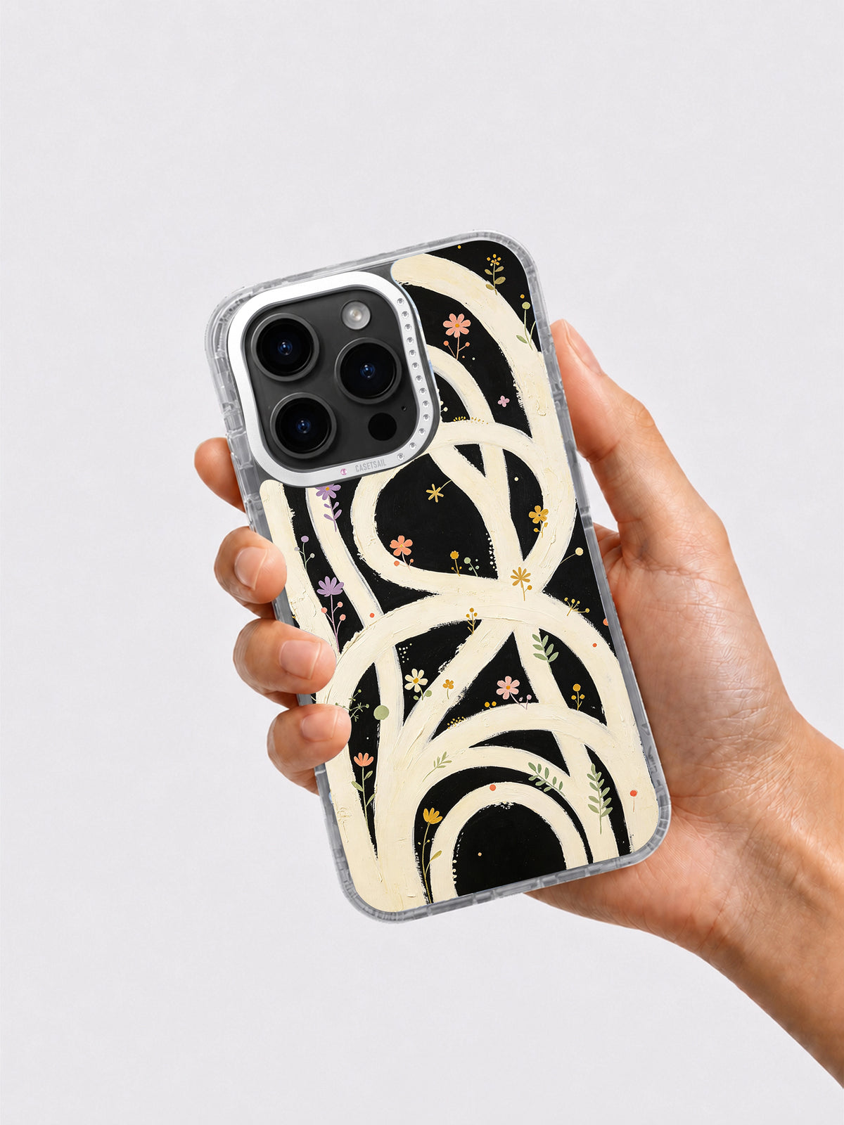 Hand holding black cream and colorful floral loop iPhone case