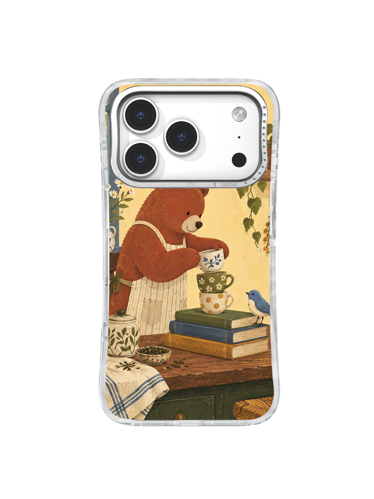 Brick-red bear arranging a floral cup on stacked books with a dusty-blue bird on an iPhone 17 Pro case