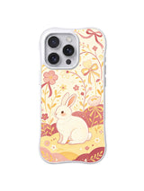 Velvet Bow Rabbit Garden / Blush Ribbon Rabbit: Kıvrımlı kurdeleler ve şeftali çiçeklerinin altında küçük açık tavşan; katmanlı pembe-sarı zemin.