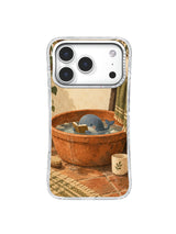 Tiny blue whale reading in a terracotta washbasin beside a cream cup on an iPhone 17 Pro case