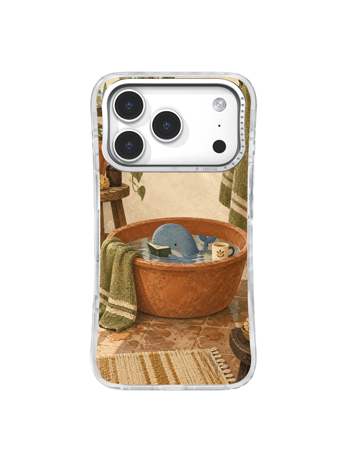 Tiny whale reading in a terracotta washbasin with an olive towel and cream cup on an iPhone 17 Pro case