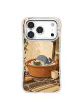Tiny blue whale and olive towel forming a soft shore inside a terracotta basin on an iPhone 17 Pro case